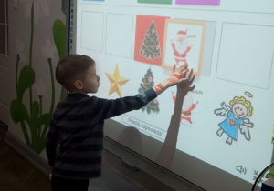 Adaś stoi przy tablicy multimedialnej i dopasowuje obrazki świąteczne do pary.