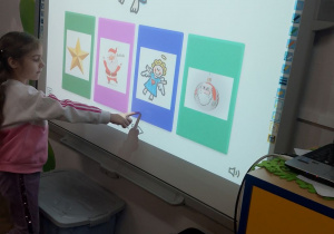 Amanda stoi przy tablicy multimedialnej i wskazuje obrazek z aniołkiem.