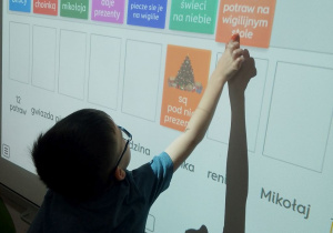 Mikołaj rozwiązuje zagadki świąteczne na tablicy multimedialnej.