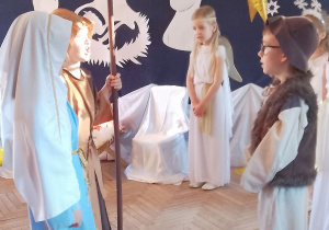 Marysia w roli Maryi i Antek w roli Józefa stoją przed Mikołajem w roli Gospodarza. W tle fragment dekoracji jasełkowej i Nikola w roli Aniołka.
