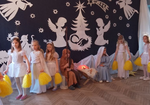 Obok żłóbka siedzi Marysia w roli Maryi i Antek w roli Józefa. Po bokach stoją Gwiazdki i Aniołki z żółtymi pomponami w rękach.