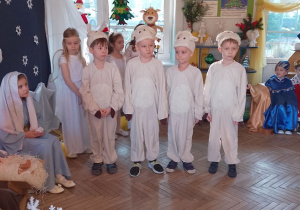 Czterech chłopców w roli Baranków stoi przy żłóbku. Obok siedzi Maryja.