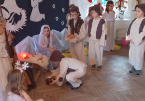 Bruno w roli Pastuszka przykucnął obok żłóbka i kładzie garnuszek ze śmietaną.