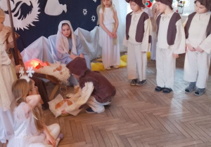 Mikołaj przykucnął obok żłóbka i kładzie bochen chleba.