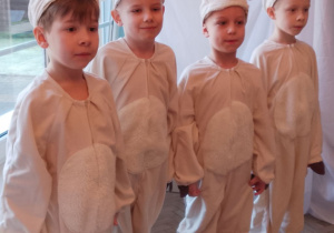 Czterech chłopców w roli Baranków stoi obok siebie podczas przedstawienia.