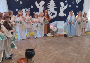 Dzieci w strojach jasełkowych stoją w półkolu trzymając upominki dla rodziców.