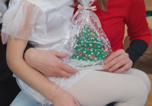 Weronika siedzi na kolanach mamy, która trzyma upominek - choinkę.