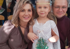 Tosia pozuje do zdjęcia z rodzicami. Dziewczynka trzyma własnoręcznie wykonaną choinkę.