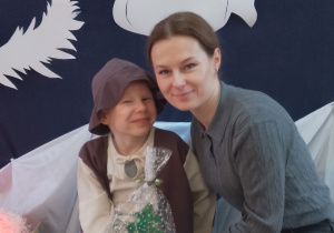 Bruno pozuje do zdjęcia z mamą na tle jasełkowej dekoracji. Rodzic trzyma upominek - choinkę.