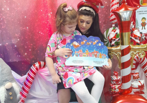 Nadia siedzi u mamy na kolanach. Pani pokazuje kolejny obrazek w książce "Idą święta".