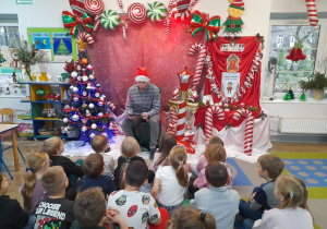 Dzieci siedzą na dywanie, a Pan Łukasz czyta opowieść pt. "Złota rybka" z książki "Najpiękniejsze opowieści pod choinkę".