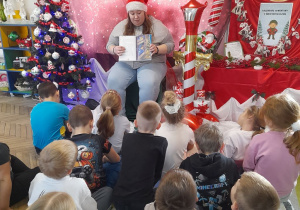 Dzieci siedzą na dywanie, a Pani psycholog prezentuje obrazek w książce. W tle dekoracja świąteczna.