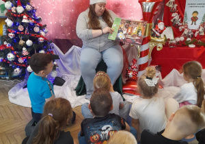 Dzieci siedzą na dywanie, a Pani Martyna pokazuje obrazek w książce "Gdzie jest w święta Bluey? Szukaj i znajdź".