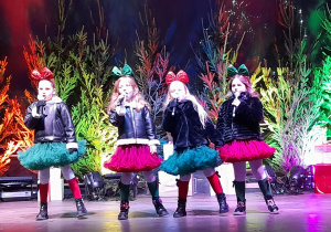 Zespół "Słoneczka" prezentuje na scenie piosenkę świąteczną. W tle drzewka świąteczne.