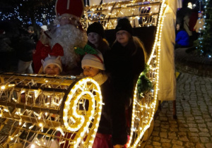 Cztery dziewczynki siedzą w saniach świątecznych obok Mikołaja.