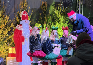 Nadia, Tosia, Emma i Marysia stoją na scenie podczas wręczania dyplomu i upominków. W tle dekoracja świąteczna, Mikołaj.