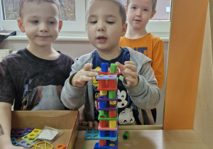 Szymek, Marcel i Julek układają wieżę z klocków Numicon.