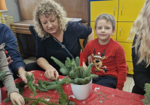 Franek wraz z mamą wkładają gałązki świerku do doniczki.