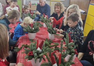 Dzieci i rodzice siedzą przy stole w trakcie pracy nad świątecznymi dekoracjami.