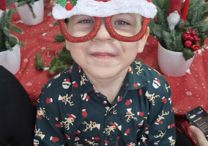 Antoś uśmiecha się do zdjęcia. Chłopic ma na sobie świąteczne okulary.