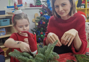 Ola z mamą siedzą przy stole i komponują stroik świąteczny.