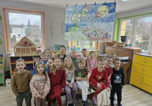 Dzieci pozują do zdjęcia. Nad nimi wisi składająca się z 16 części kolorowanka z wizerunkiem Grincha.