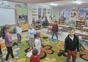 Dzieci sprzątają rozrzucone przez Grincha na dywanie klocki i kredki.