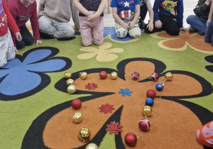 Na dywanie leży ułożona z bombek choinka, w tle widać dzieci z grupy Biedronek.