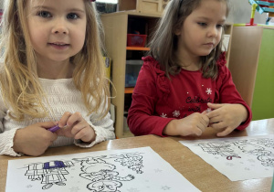 Ala i Klara siedzą przy stoliku i kolorują kolorowanką.