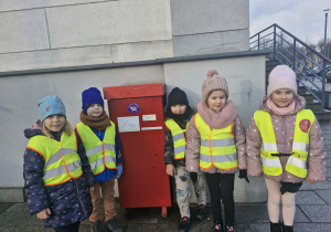Grupa dzieci stoi obok skrzynki pocztowej.