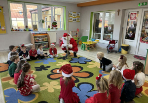 Dzieci siedzą w kole, Święty Mikołaj zadaje im pytania, dotyczące Świąt Bożego Narodzenia.