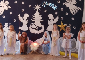 Maryja z Józefem siedzą obok żłóbka. Obok stoją dziewczynki w roli Aniołków i Gwiazdki. Maryja trzyma lalkę (Jezuska) na ręku i śpiewa kołysankę.