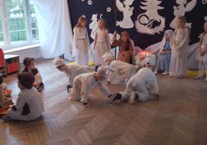 Czterech chłopców w roli Baranków idzie na kolanach w małym kółeczku. W tle dekoracja oraz dzieci w roli Aniołów, Gwiazdki, Maryi, Józefa. Z lewej strony przy ognisku siedzą Pastuszkowie.