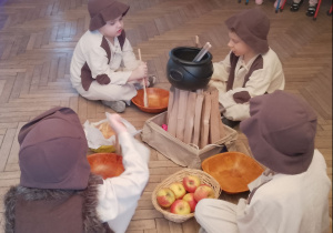 Czterech Pastuszków siedzi przy ognisku i przy pastorałce "Chojka" miesza w miskach drewnianymi łyżkami.