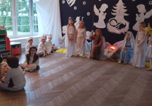Dzieci podczas przedstawienia śpiewają pastorałkę "Stajenka nasza licha". Przy żłóbku siedzą Maryja i Józef, a obok stoją dziewczynki w roli Aniołków i Gwiazdki. Z lewej strony siedzą chłopcy w roli Baranków i Pastuszkowie wokół ogniska. W tle dekoracja jasełkowa