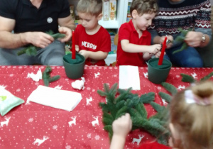 Olaf z tatą i Michał z mamą ozdabiają świąteczny stroik.