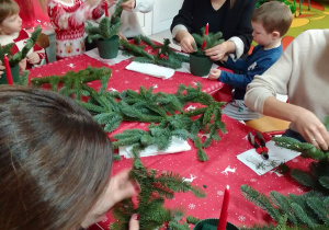 Ala z mamą i Michał z mamą ozdabiają świąteczny stroik jodłowymi gałązkami.