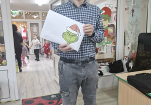 Pan Łukasz stoi w drzwiach Sali Biedronek i trzyma w dłoniach dużą kopertę z wizerunkiem Grincha.