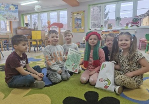 Dzieci siedzą na dywanie trzymając w dłoniach list od Grincha i dużą kopertę pełną cukierków.