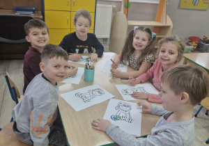 Przedszkolaki siedzą przy stoliku i kolorują kolorowanki z wizerunkiem Grincha.