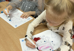 Alicja i Marysia siedzą przy stoliczku. Dziewczynki kolorują karty pracy.