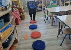 Wojtuś skacze po kołach zgodnie ze strzałkami leżącymi na podłodze.