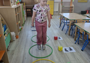 Weronika stoi w dużej obręczy. Obok obręczy leżą kostki do gry oraz rysunki z jedną lub dwiema stopami.