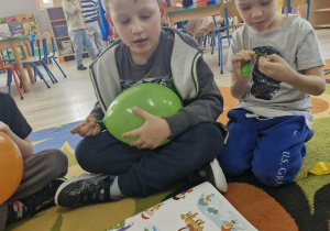 Franek i Ignaś oglądają plakat przedstawiający sporty zimowe. Franek trzyma w dłoniach zielony balon.