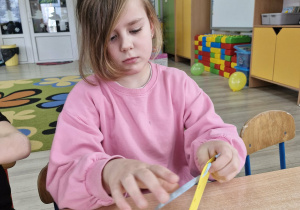 Weronika nawleka niebieską wstążkę na żółty kartonik.