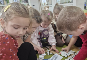 Przedszkolaki siedzą na dywanie i układają puzzle - drogi do ozobotów.