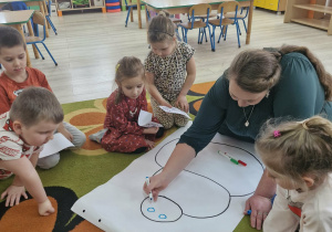 Pani z biblioteki rysuje dzieciom dużego bałwana na białym kartonie.