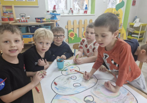 Przedszkolaki kolorują rysunek bałwana.