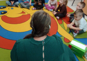 "Pszczółki" zgromadzone na dywanie słuchają Pani z biblioteki, która opowiada dzieciom o Ozobotach.