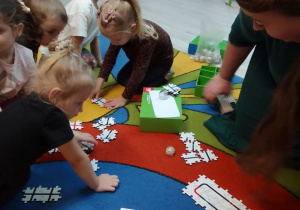 Pani z biblioteki i grupa "Pszczółek" układają z elementów trasę dla Ozobotów.